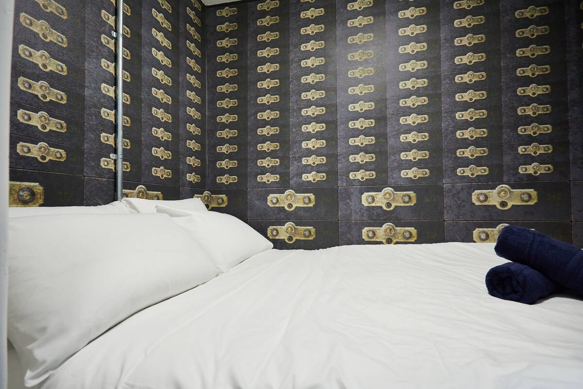 Una habitación de hotel con una cama, ropa de cama blanca y una pared con un motivo repetido de cerraduras doradas.