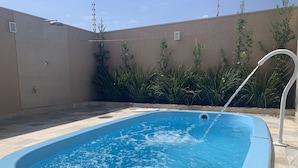 A rectangular swimming pool with a water fountain feature, surrounded by a tiled patio and a low wall with greenery. - (Olímpia)