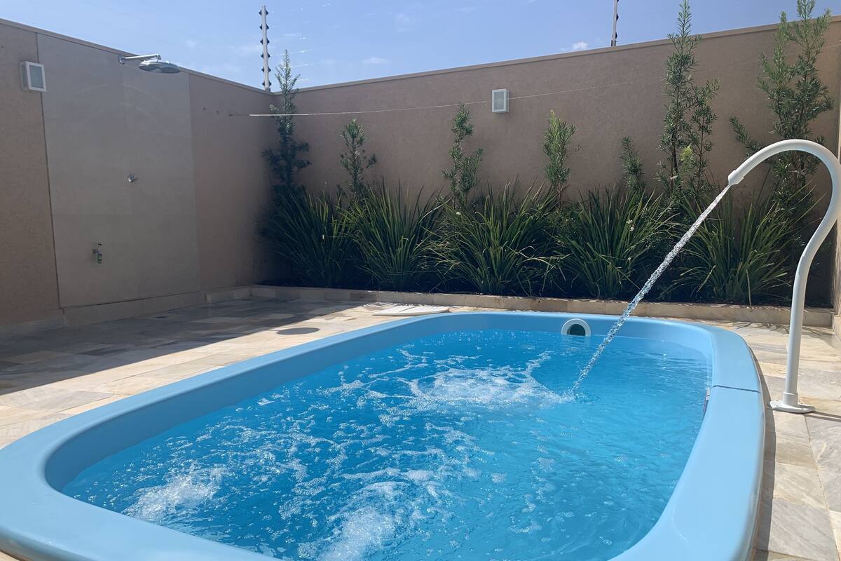 Une piscine rectangulaire agrémentée d’une fontaine, entourée d’une terrasse carrelée et d’un petit muret orné de verdure.