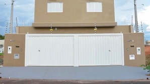 A two-story building with a flat roof, two air conditioning units on the upper level, and a double garage door. - (Olímpia)