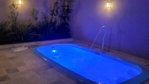 A swimming pool with a blue light, surrounded by plants and a stone floor. - (Olímpia)