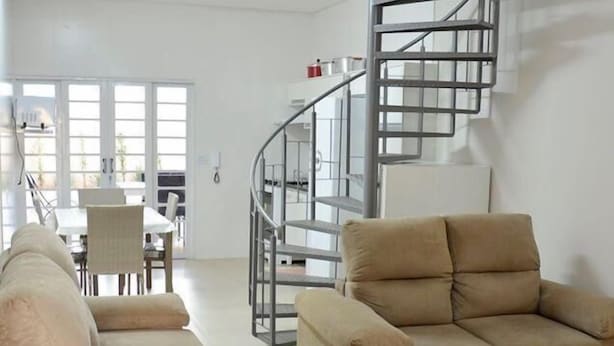 A spacious living room with a beige sofa, a tan armchair, and a spiral staircase. - (Olímpia)
