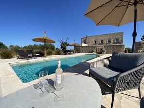 Zona junto a la piscina con sillones de descanso, una mesa con copas de vino y una botella.