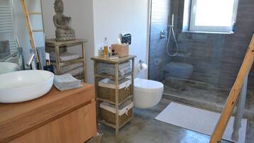 Un baño con tocador de madera, un lavabo blanco grande, un inodoro y una zona de ducha.