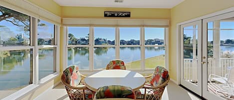 Enjoy a serene view of the water from this room's large window, featuring a ceiling fan, a table with four chairs, and access to an outdoor area.