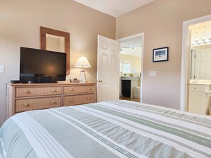 Ein Schlafzimmer mit Bett, Fernseher, Kommode und einer Tür zum Badezimmer.