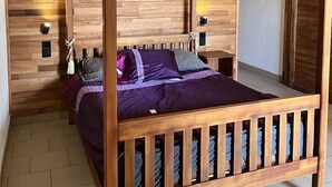 Ein Himmelbett mit Holzrahmen und einer violetten Bettdecke, vor einer Holzwand mit Schliffmuster.