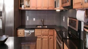 A kitchen with wooden cabinets, a black countertop, stainless steel appliances, and a ceiling fan.