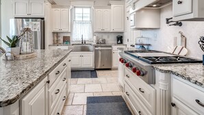 Una cocina moderna con armarios blancos, encimera de granito, electrodomésticos de acero inoxidable y una lámpara colgante.