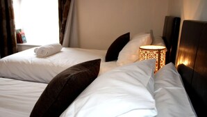 A hotel room with two beds, white linens, dark brown pillows, and a bedside lamp. - Cotswolds Valley Accommodation-Excl Prop (Stroud)