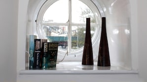 A window with a view of buildings outside, a bookshelf with books, and two decorative vases. - Cotswolds Valley Accommodation-Excl Prop (Stroud)