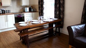 A dining area with a wooden table set for four, a microwave, and a toaster on the counter. - Cotswolds Valley Accommodation-Excl Prop (Stroud)