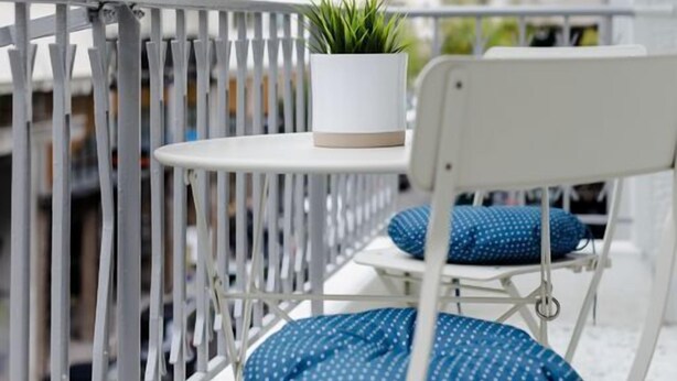 A balcony with a white metal railing, a small table with a potted plant, and two blue polka-dotted chairs.