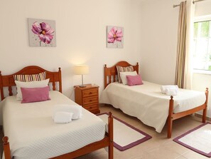Two single beds with white bedding and pink pillows, a wooden nightstand, and floral artwork create a cozy retreat.