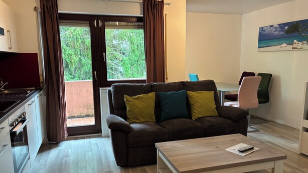 A living room with a sofa, a coffee table, a TV, and a dining area with chairs. - 3 Room Appartment (70 m2) with 2 Bedrooms, Balcony & Garage (Neckarsulm)