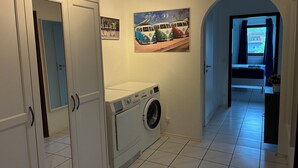 A laundry room with a washing machine, a drying rack, and a door leading to another room. - 3 Room Appartment (70 m2) with 2 Bedrooms, Balcony & Garage (Neckarsulm)