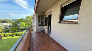 A balcony with a tiled floor, a chair, and a window overlooking a parking area and greenery. - 3 Room Appartment (70 m2) with 2 Bedrooms, Balcony & Garage (Neckarsulm)