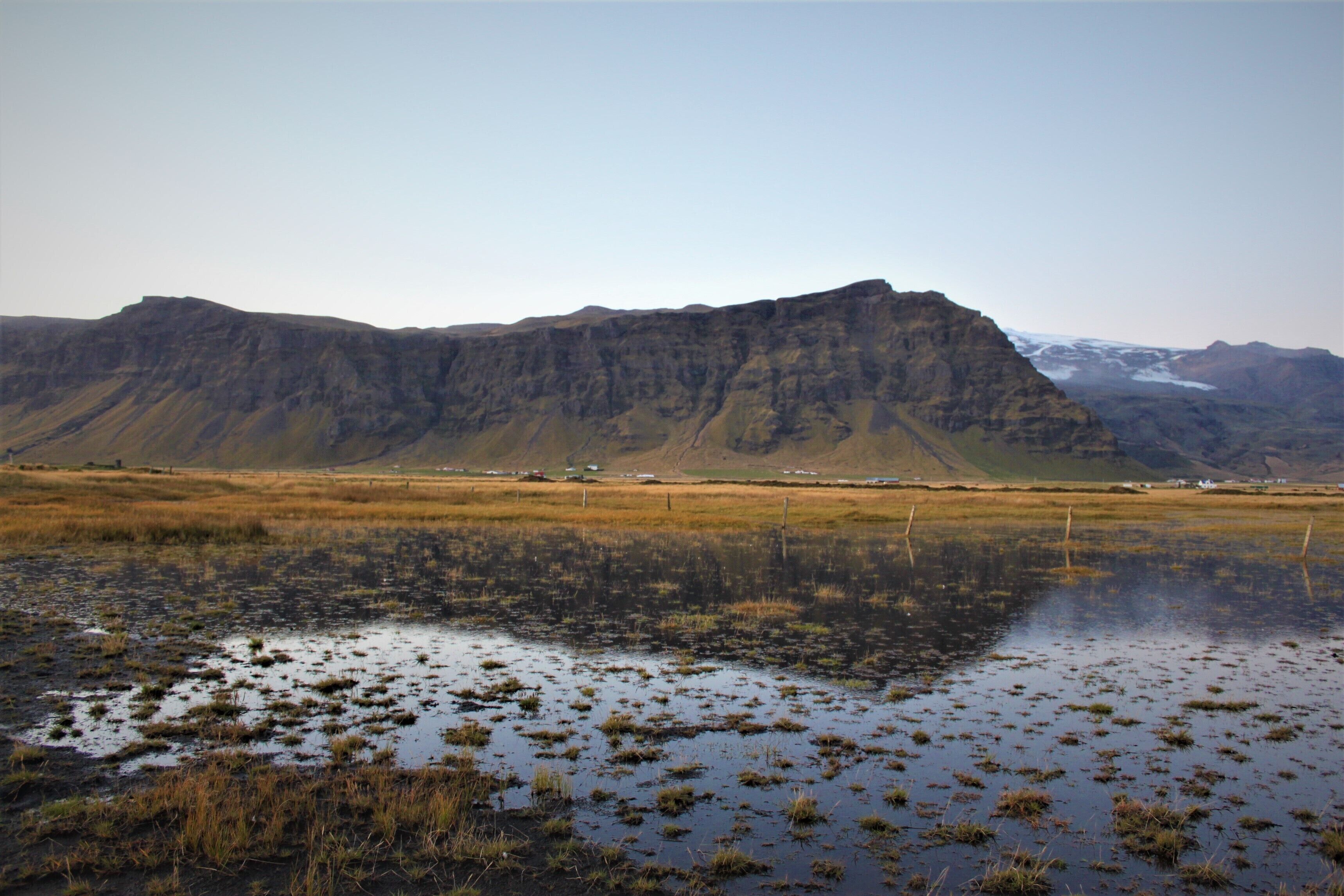 A flat landscape with a large mountain in the background and a body of water in the foreground.