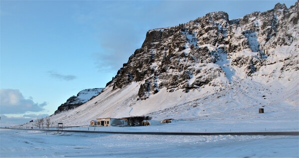 A snow-covered landscape with a mountain, a road, and a few buildings.