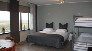 A modern hotel room with a large bed, a bunk bed, a dining table, and a view of the desert through the window.