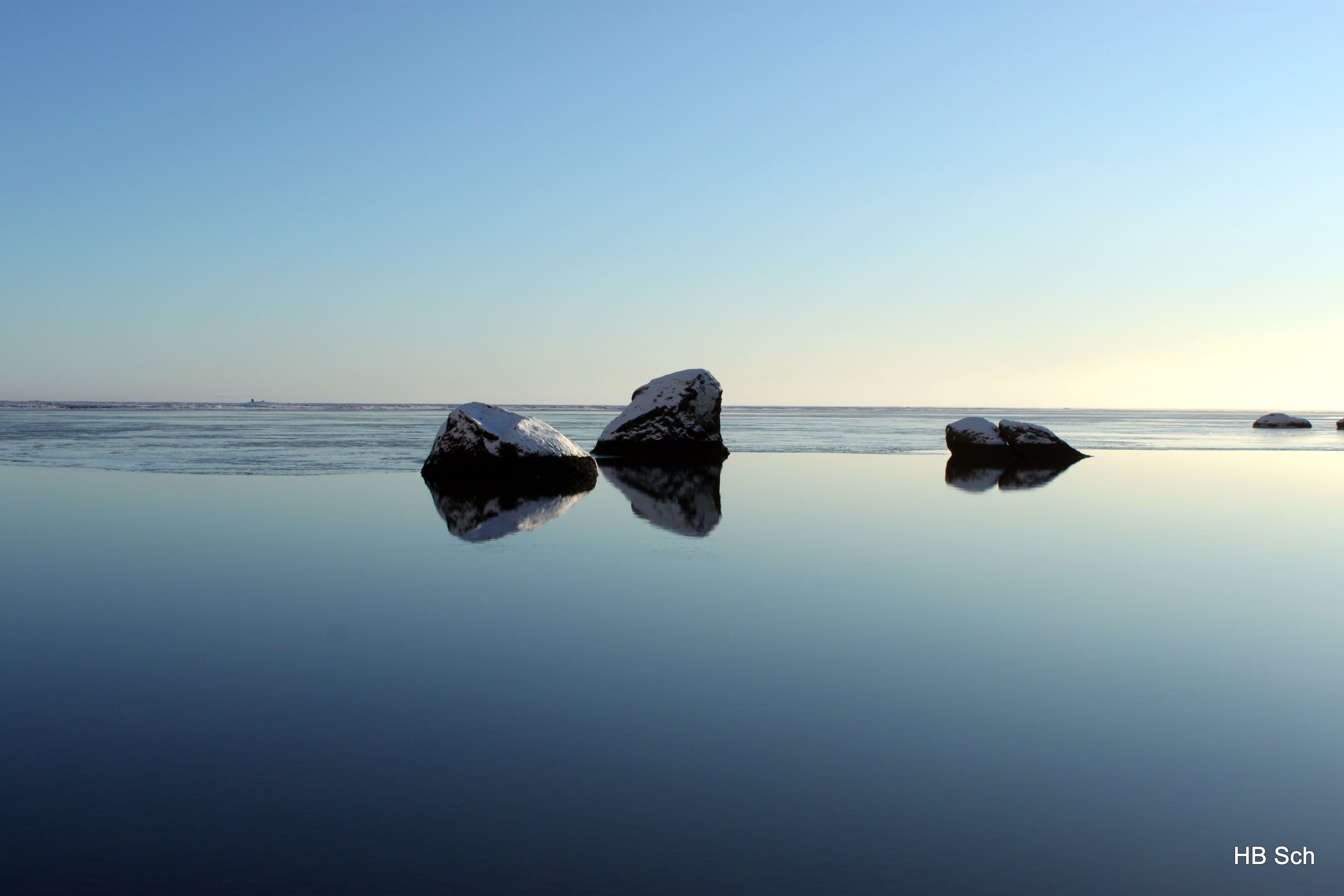 A calm body of water with three large rocks.