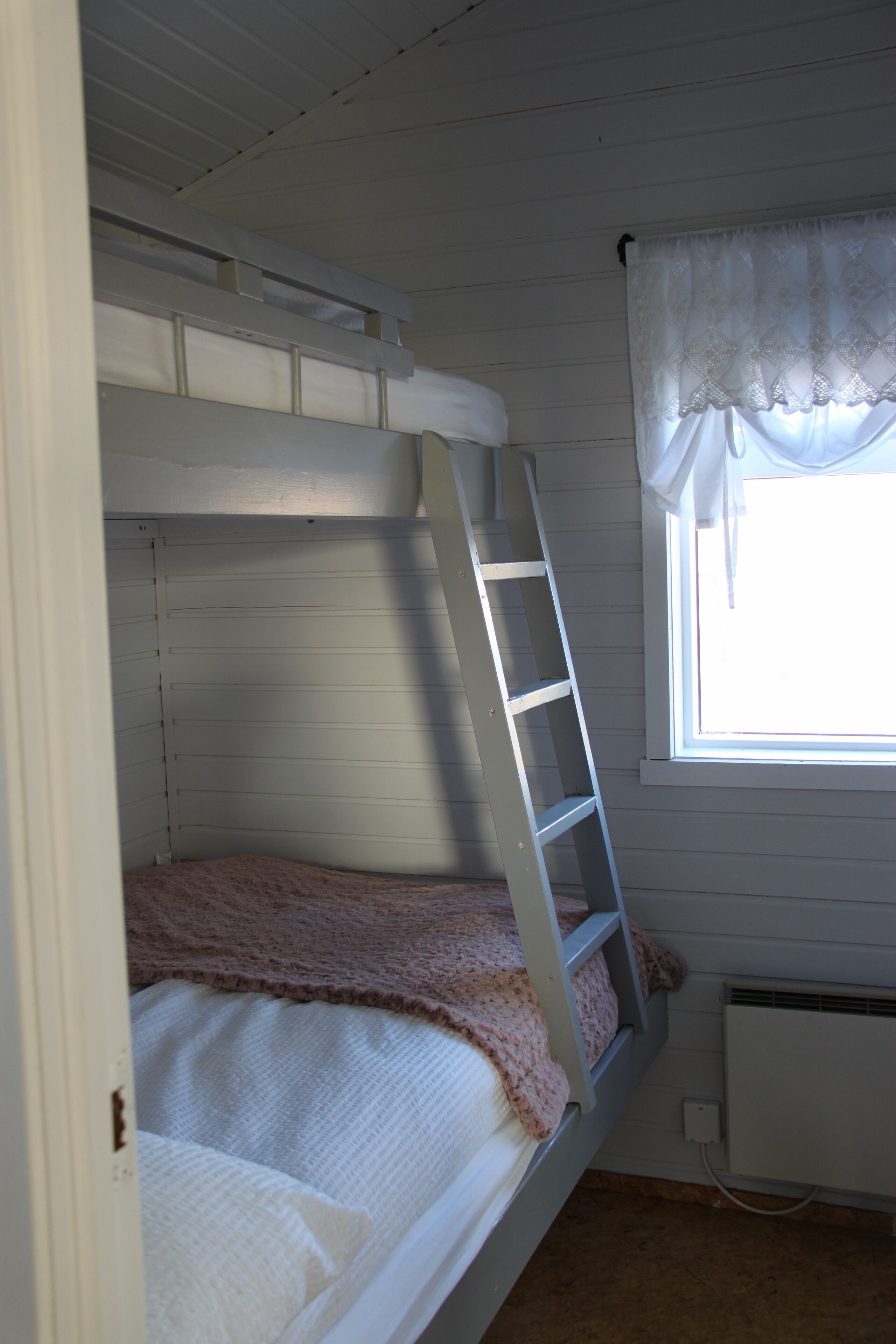 A bunk bed with a ladder, a window with a white valance, and a radiator.
