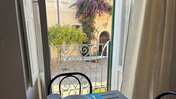 Ein Balkon mit Tisch für zwei Personen, Blick auf ein Gebäude mit der Aufschrift 'MUNICIPIO' und einem Metallgitter.