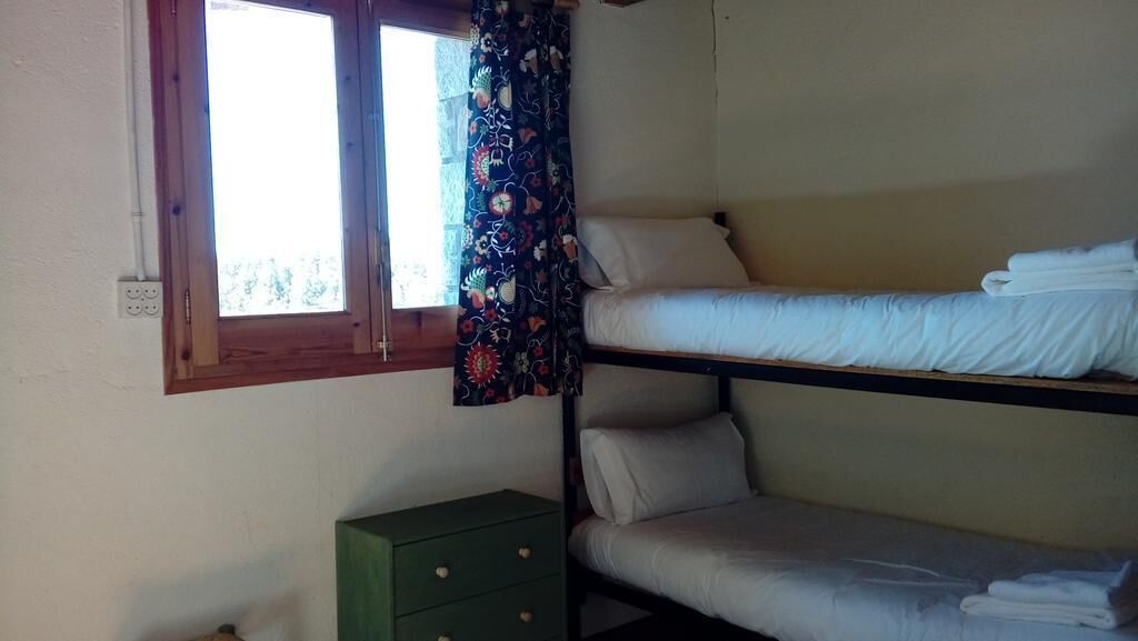 Une chambre de dortoir avec des lits superposés, une fenêtre avec un rideau et une commode verte.