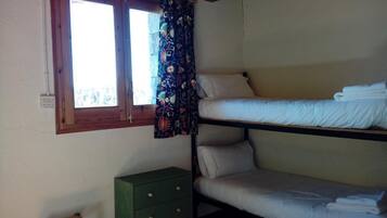 Une chambre de dortoir avec des lits superposés, une fenêtre avec un rideau et une commode verte.