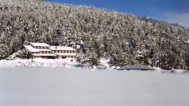A snow-covered lodge with a symmetrical facade and a flat roof, surrounded by dense forest. - Refugi Cap del Rec - Hostel (Lles)
