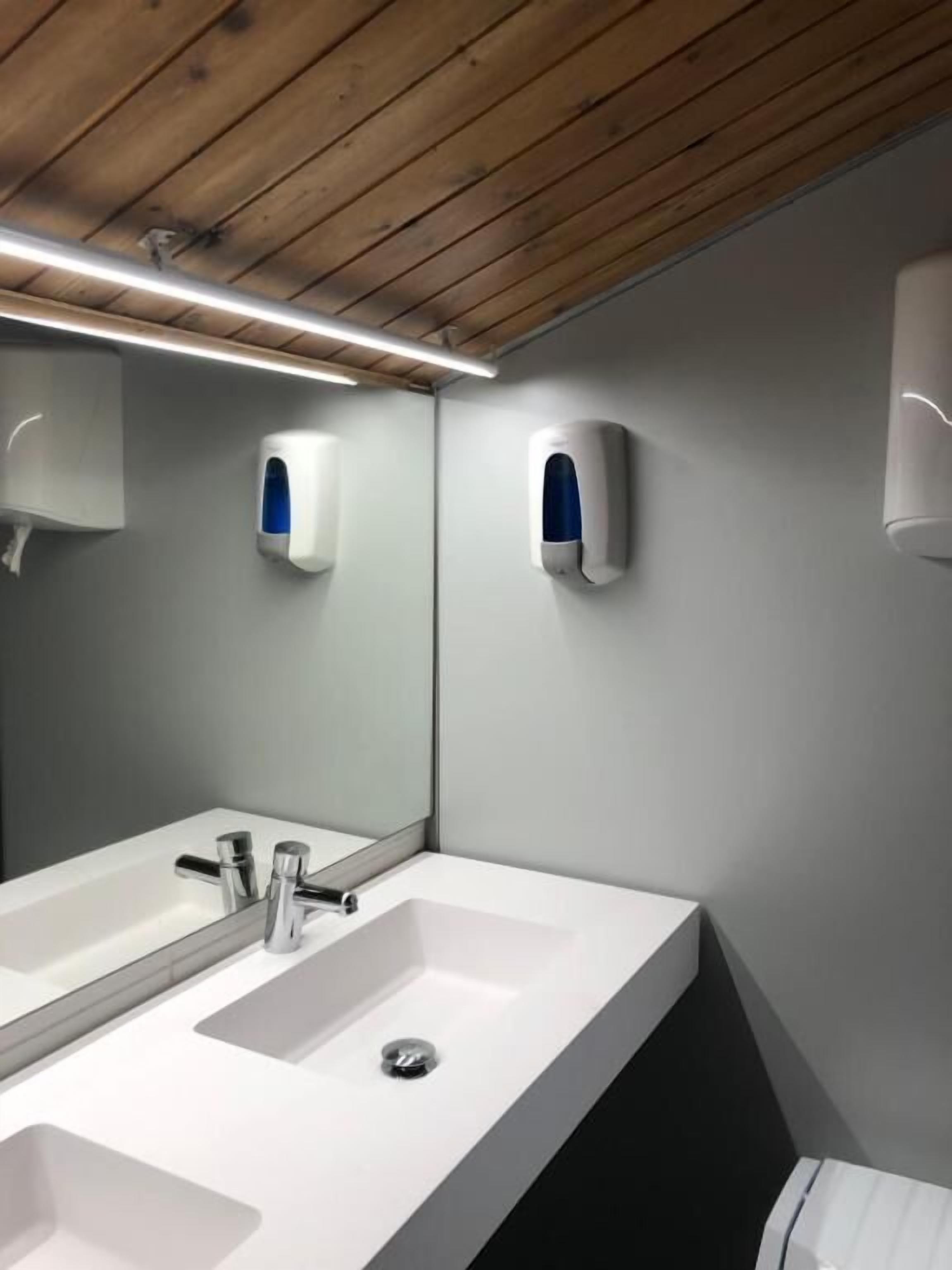 Un baño moderno con un espejo grande, dos lavamanos y dispensadores de jabón de pared.
