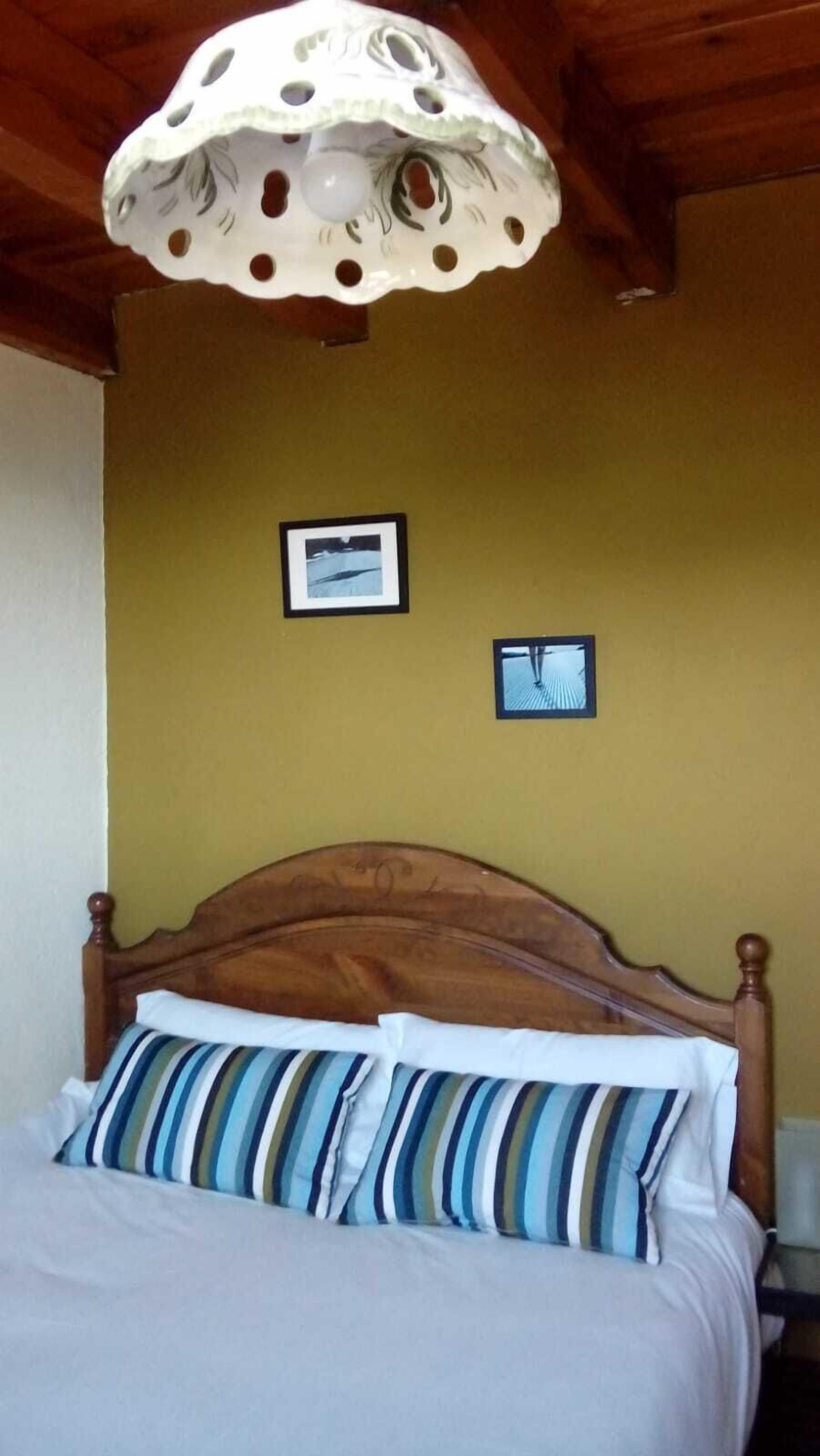 Un dormitorio con una cama de madera, almohadas a rayas, techo de madera y dos cuadros en la pared.