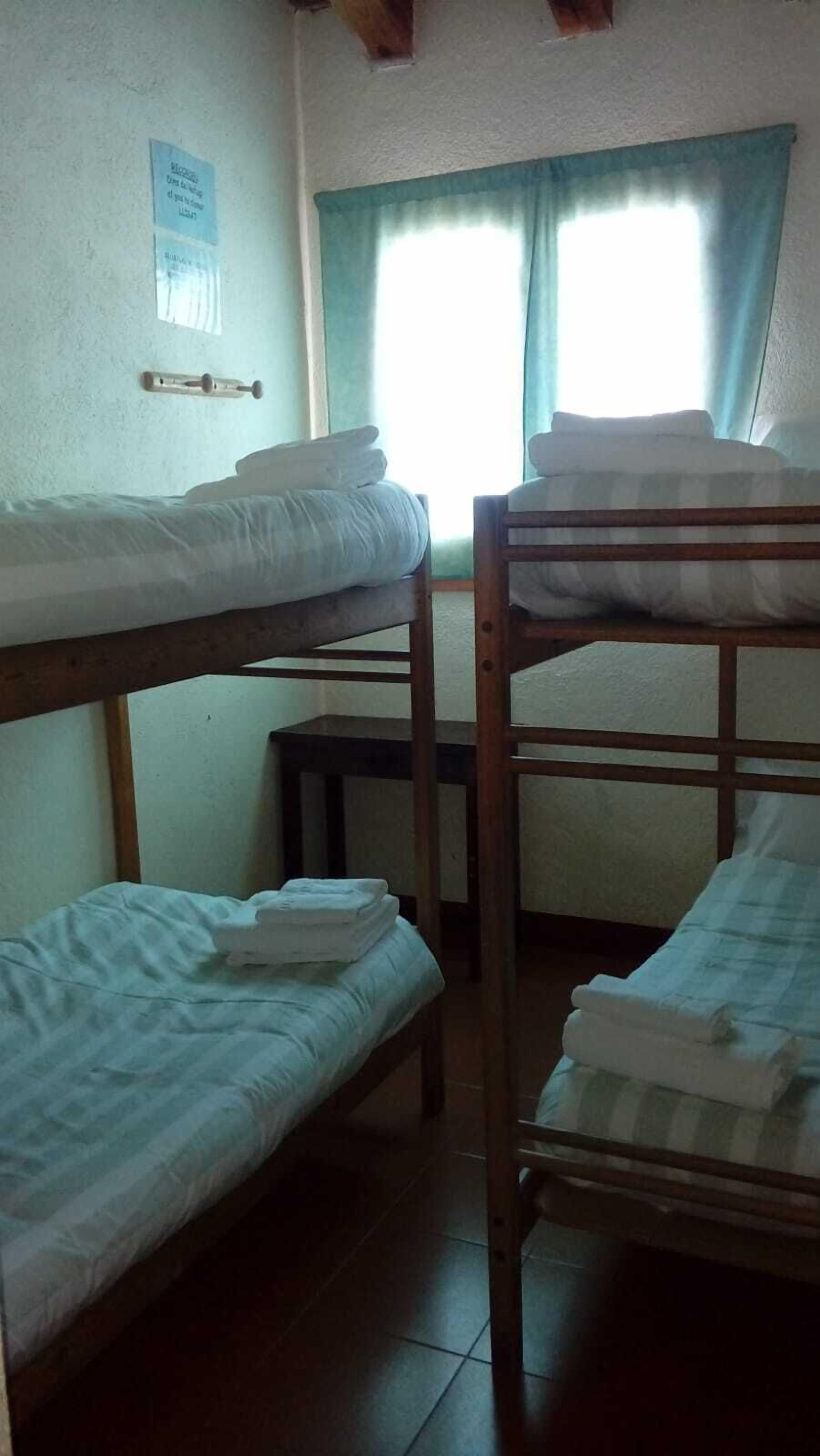 A dormitory room with bunk beds, a small table, and a window with curtains.
