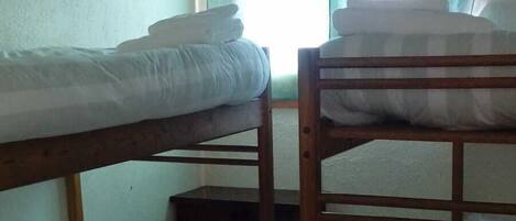 A dormitory room with bunk beds, a small table, and a window with curtains.