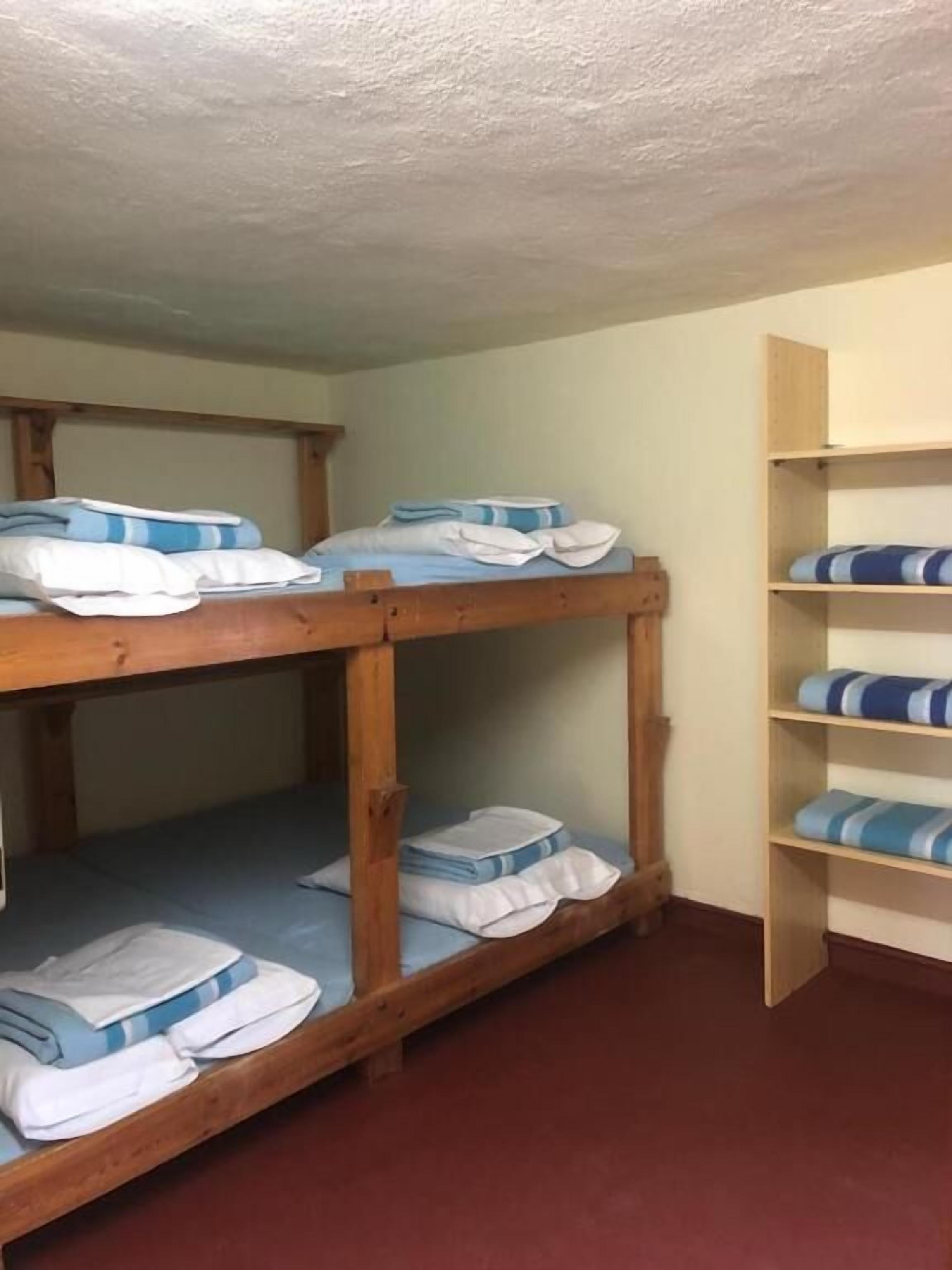 A bunk bed with blue and white bedding, a wooden shelf unit, and a red floor.