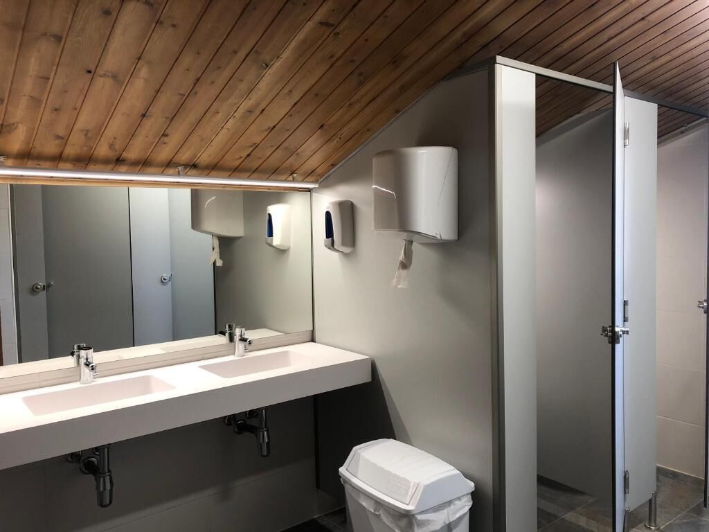 Un baño moderno con techo de madera, un lavamanos alargado con dos grifos, un espejo y un cubo de basura.