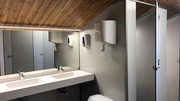 Un baño moderno con techo de madera, un lavamanos alargado con dos grifos, un espejo y un cubo de basura.