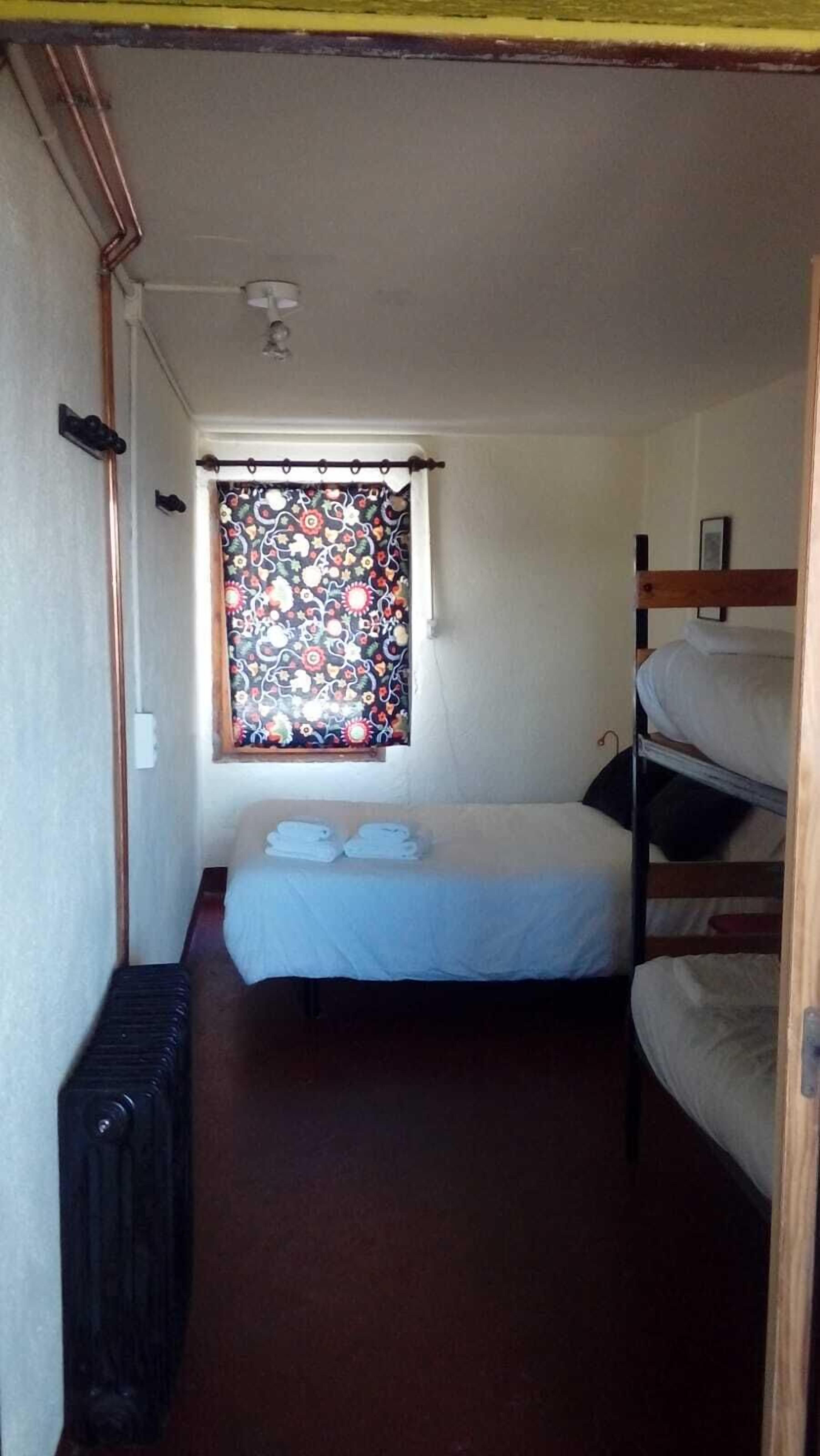 A narrow room with a bunk bed, a radiator, and a window with a floral curtain.