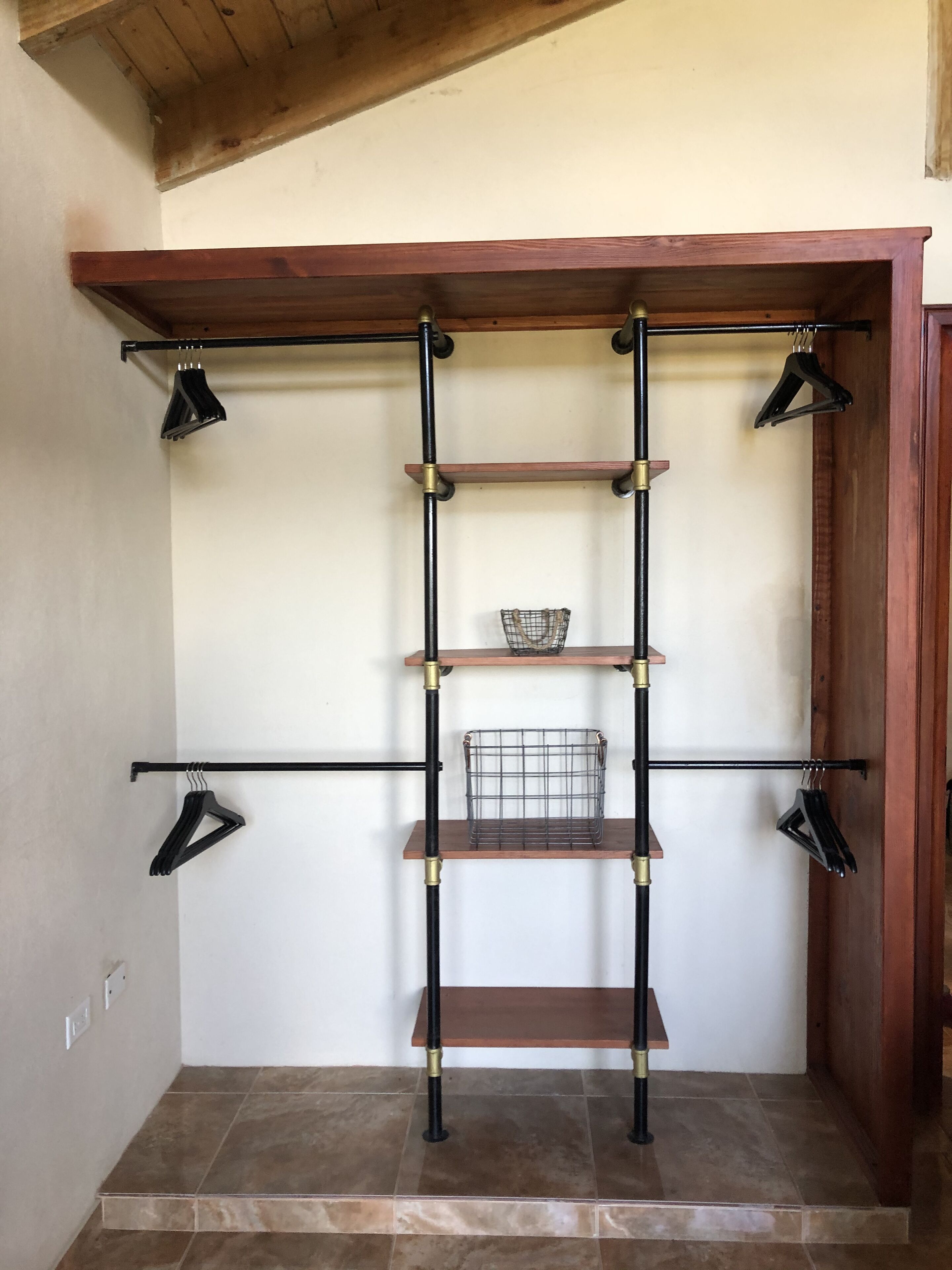 A room with a wooden ceiling, a black metal shelving unit with three shelves, and a wire basket on the middle shelf.
