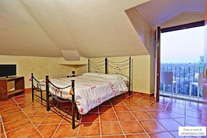 A bedroom with a bed, a desk, a chair, and a balcony with a view. - Casale del Vento (Aprilia)