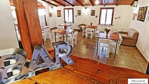 A spacious dining area with wooden tables and chairs, a wooden ceiling, and artwork on the walls. - Casale del Vento (Aprilia)