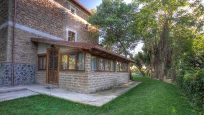A stone building with a wooden door and windows, surrounded by a well-maintained lawn and trees. - Casale del Vento (Aprilia)