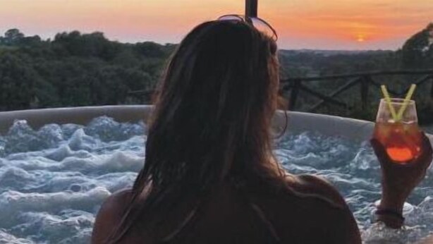A person relaxing in a hot tub with a drink, overlooking a scenic landscape during sunset. - Casale del Vento (Aprilia)