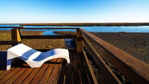 Una terraza de madera con una silla lounge blanca que da a un paisaje costero.