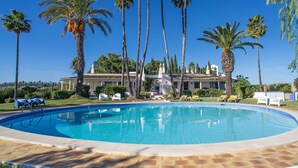 Una piscina rodeada de palmeras y sillas de descanso, con un edificio al fondo.