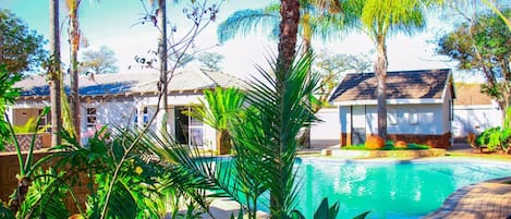 A swimming pool surrounded by lush greenery and palm trees, with a building in the background.