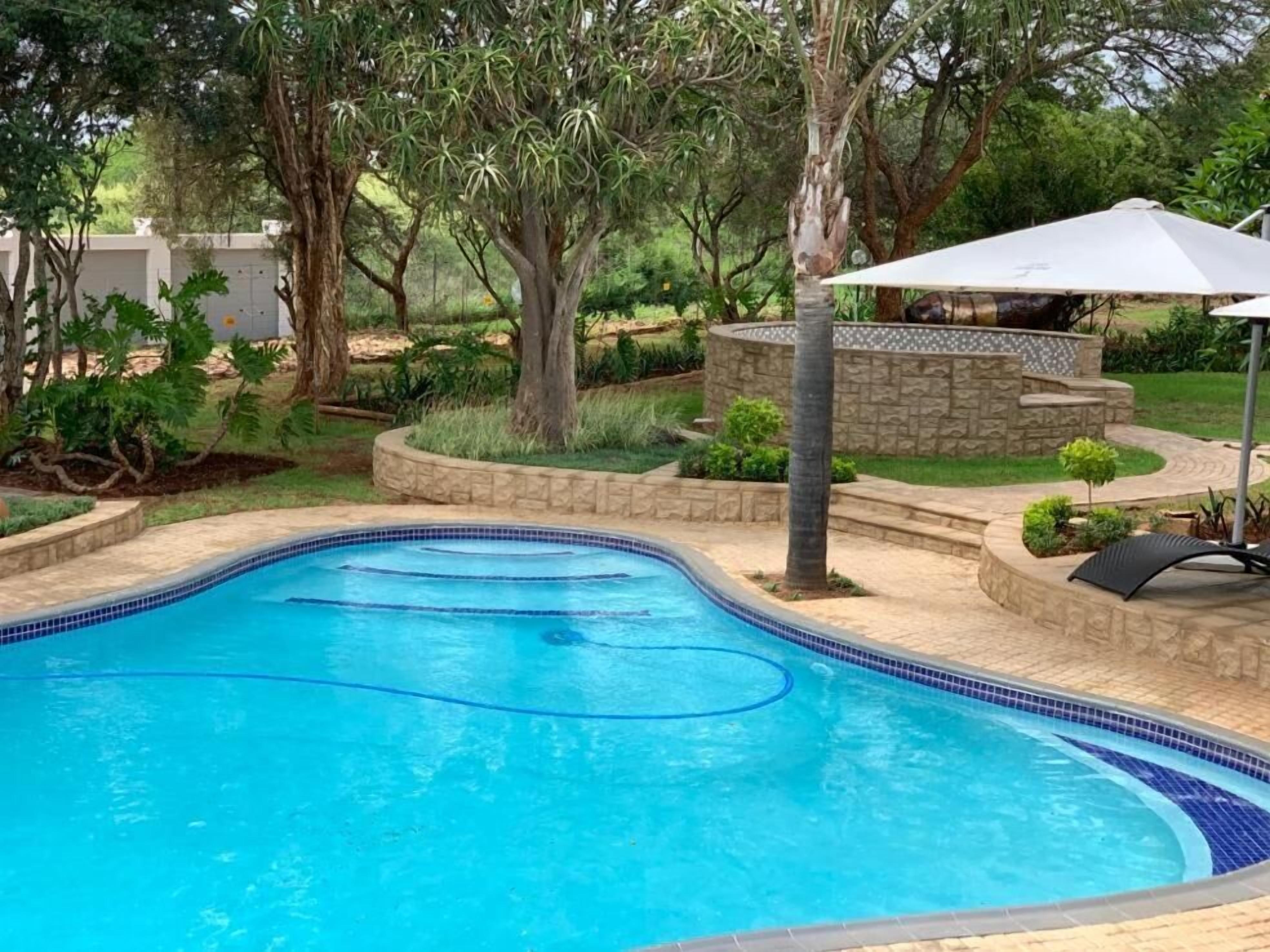 Una piscina con borde de azulejos, rodeada de un jardín ajardinado con árboles y un muro de piedra.