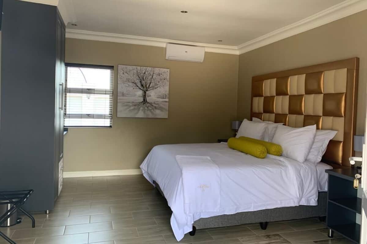 Een slaapkamer met een bed, een hoofdbord, een raam met zonwering, een wandairconditioner en een schilderij.
