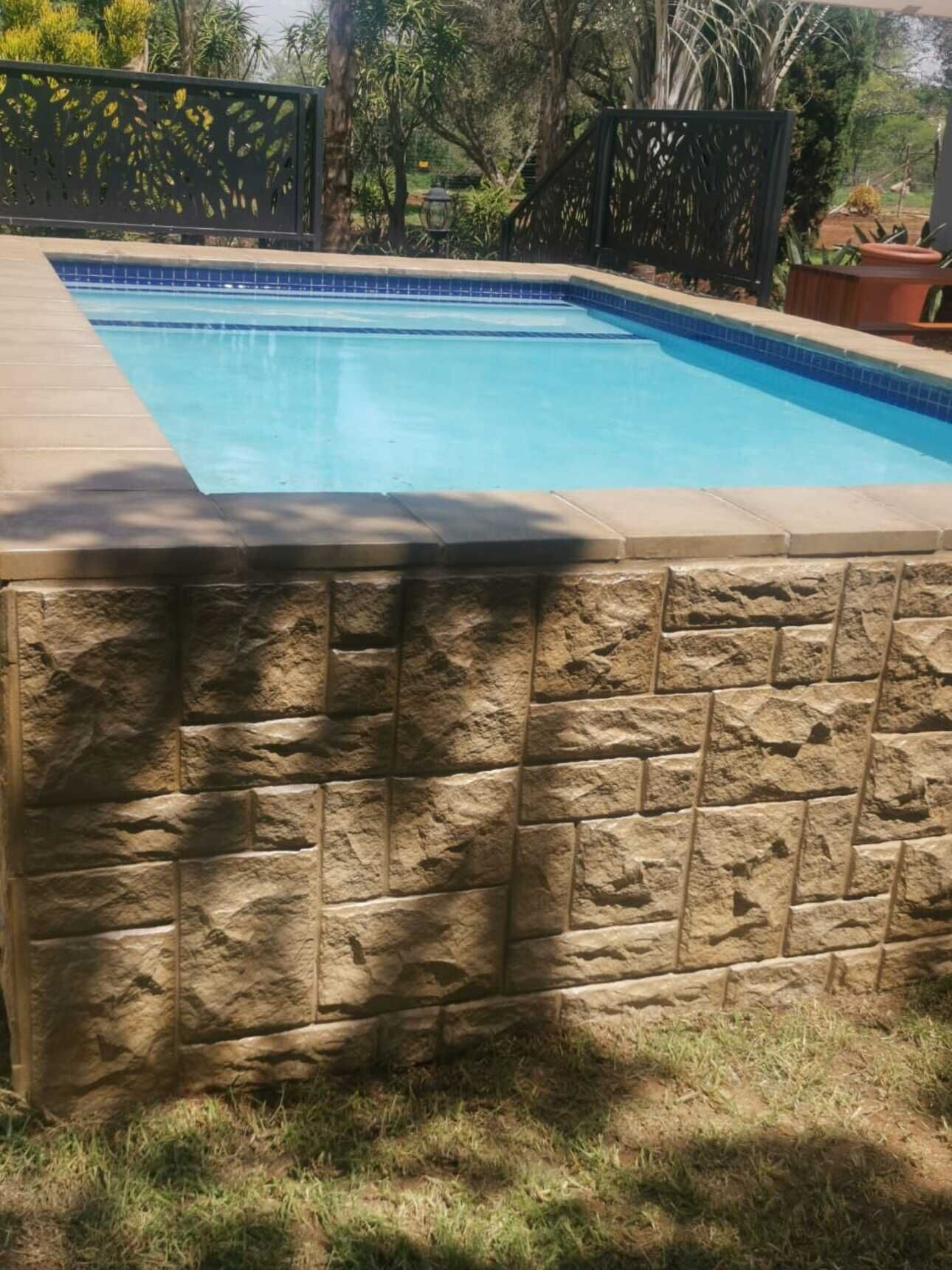 Une piscine avec un mur en pierre et une clôture en métal.