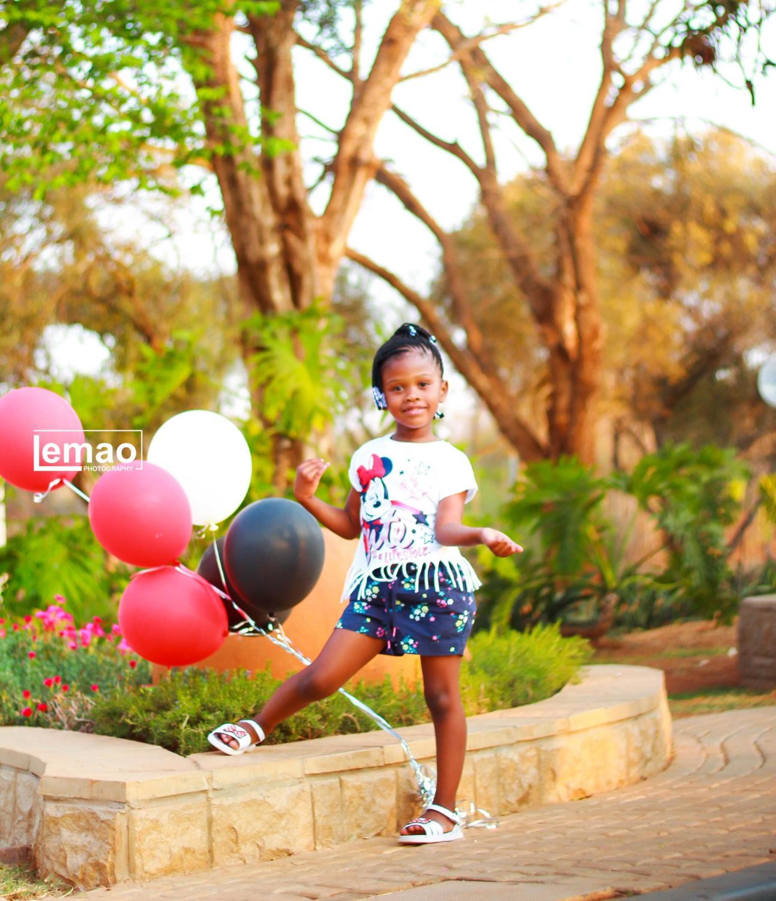Un enfant tenant des ballons dans un jardin.